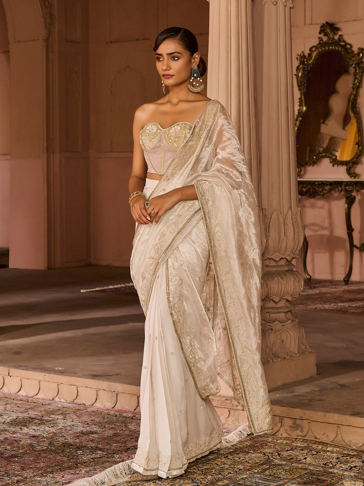Woman in a traditional silver tissue saree standing in an elegant indoor setting.